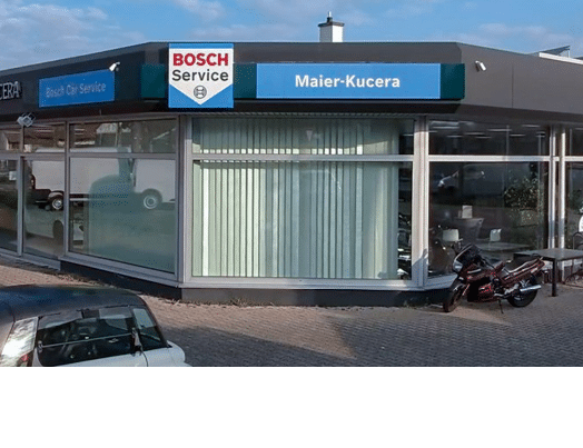 Ein Geb udefront mit den Schildern Citro n, D HER KUCERA und Bosch Car Service unter einem bew lkten Himmel. Beschreibung von KI generiert